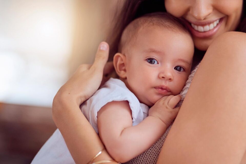 Primo piano di una madre che abbraccia il suo neonato, simbolo dell'importanza dell'immunizzazione e di come i vaccini funzionano per proteggere ogni generazione.